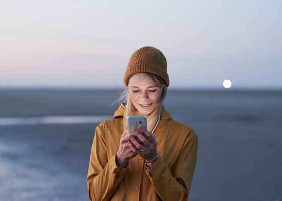 Kvinna håller i sin mobiltelefon, havet i bakgrunden