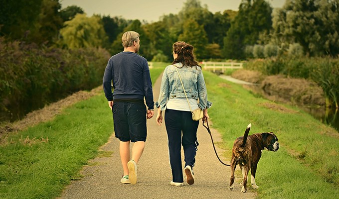 Två personer går en promenad med hund